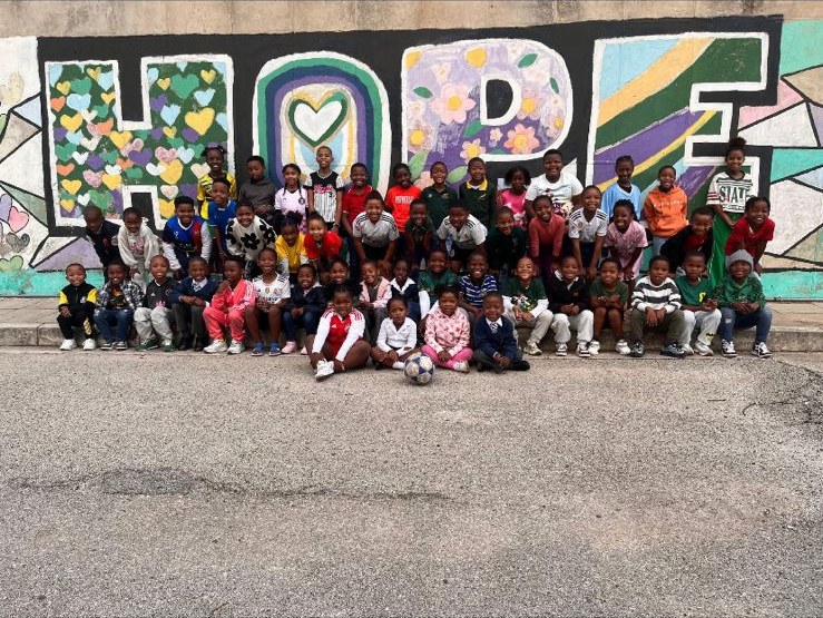 A large group of EduPlanet learners gathered in front of the painted HOPE mural.