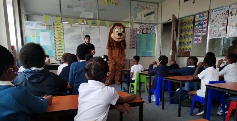 Learners seated at their desks during a classroom visit from the school mascot.