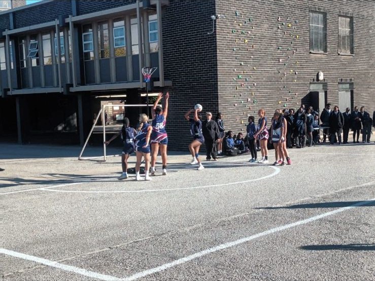 An EduPlanet netball team shooting for goal during a match on the school court.